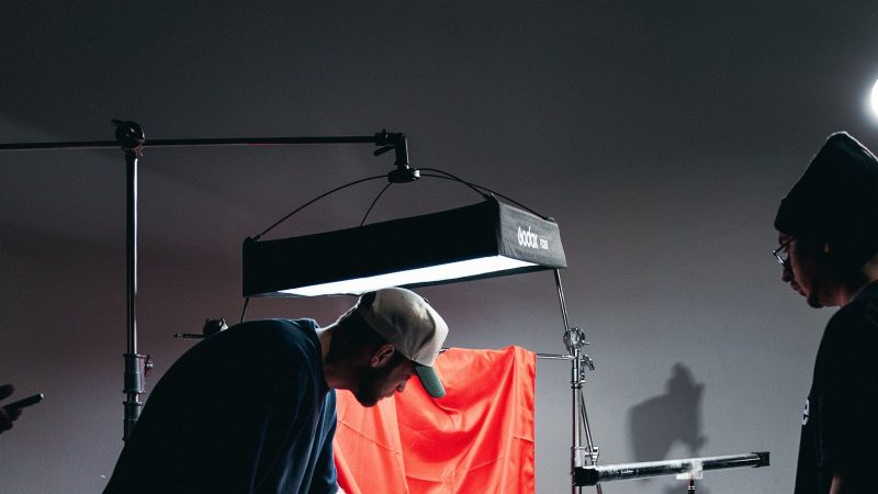 Bastidores de um set de filmagem profissional, com câmera, monitor de vídeo e iluminação de estúdio